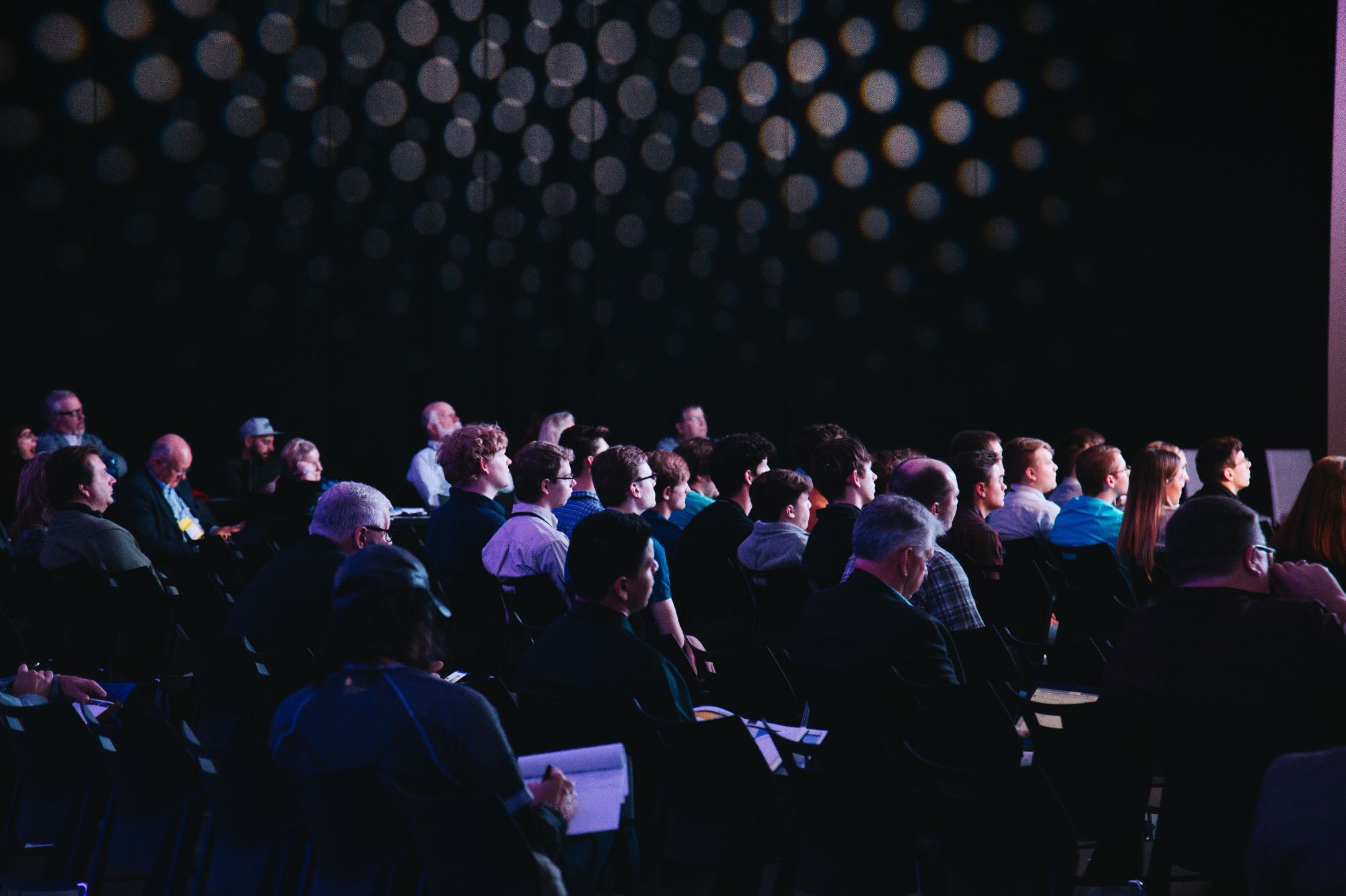 People attending a conference in a darkened auditorium